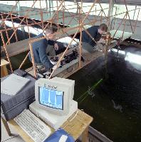 Two men set up an experiment in a water tank for what is likely a fluid dynamics experiment.  A laser is used in the water - possibly for particle image velocimetry / PIV.  What looks like an oil platform is set up above the water for some unknown testing.  10 images.